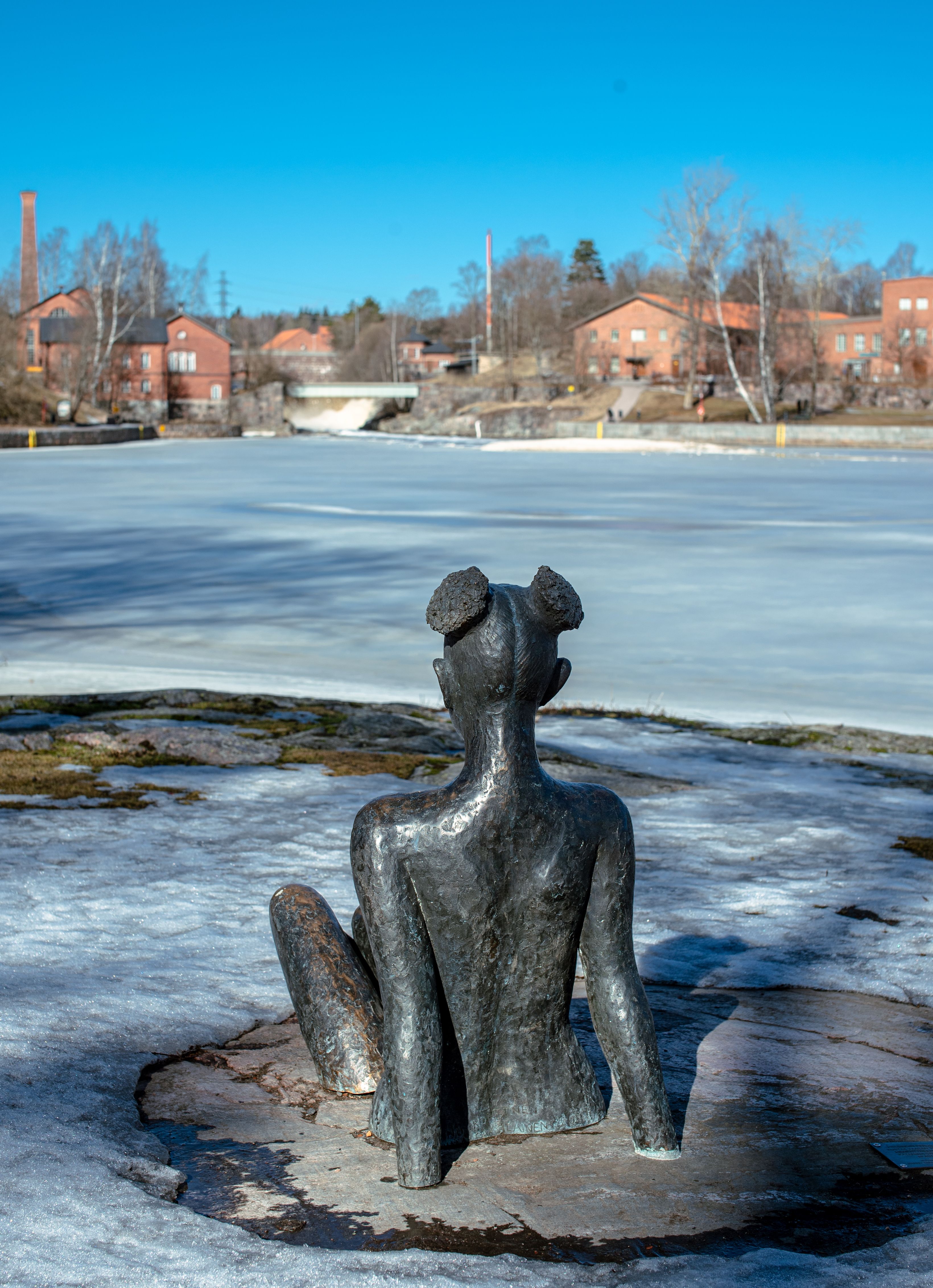 A bronze sculpture sits by a frozen river in Helsinki's old town during winter.
