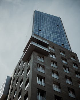 High angle view of a modern skyscraper against a cloudy sky, featuring glass and concrete architecture.