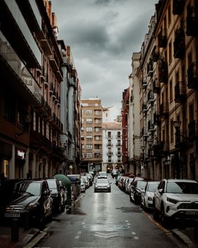A city street lined with parked cars on a rainy day, showcasing classic urban architecture.