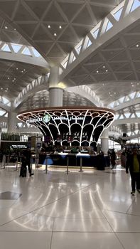 Spacious airport interior featuring a central Starbucks kiosk under geometric ceiling design.