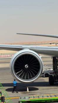 A detailed view of a commercial airplane jet engine with a technician nearby on the tarmac.