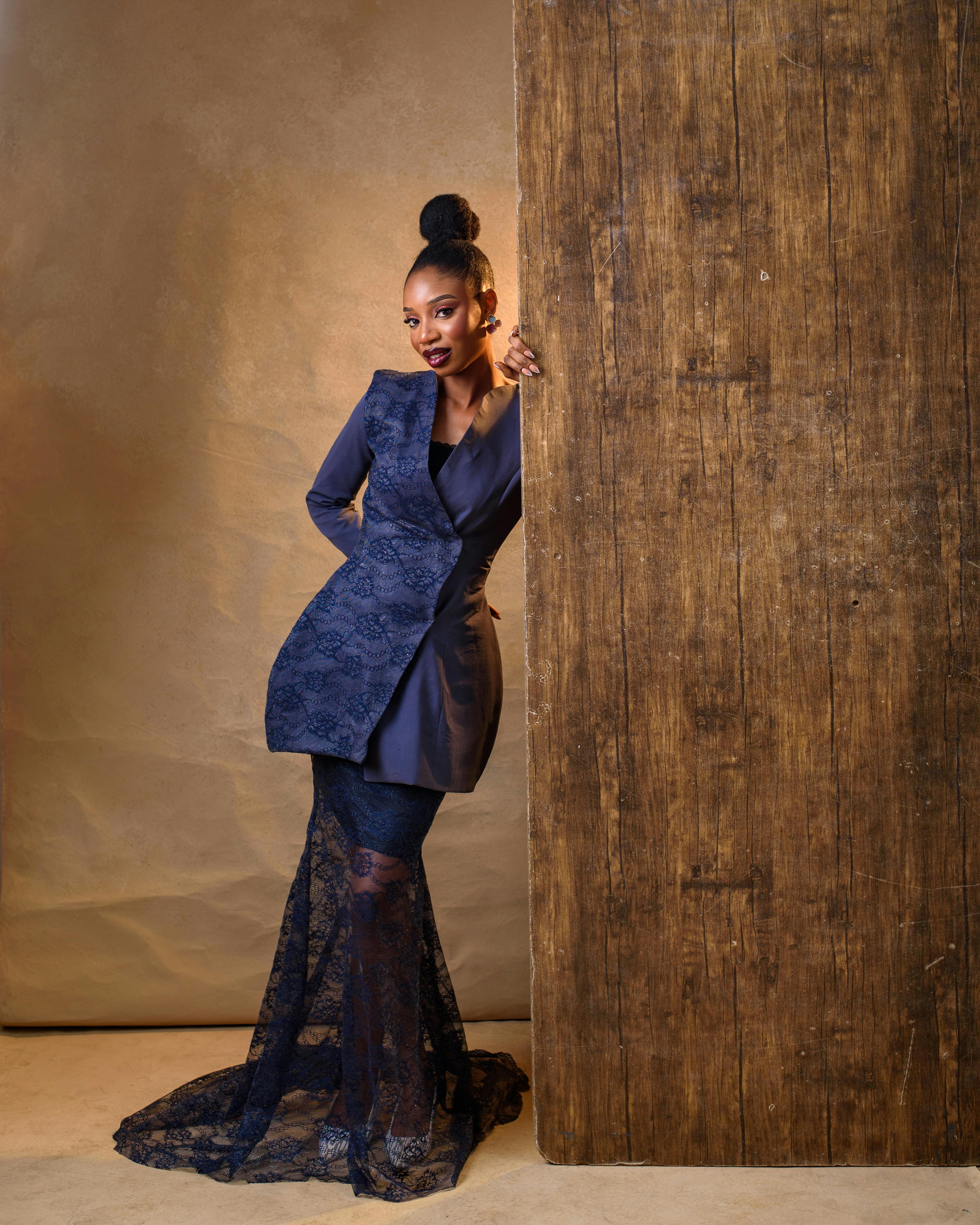 Kostenlos Eine wunderschöne Frau posiert stilvoll in einem blauen Spitzenkleid in einem Innenraum mit warmem Licht. Stock-Foto