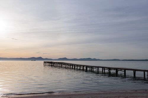 Free A peaceful sunrise over a tranquil sea with a wooden dock stretching into the water. Stock Photo