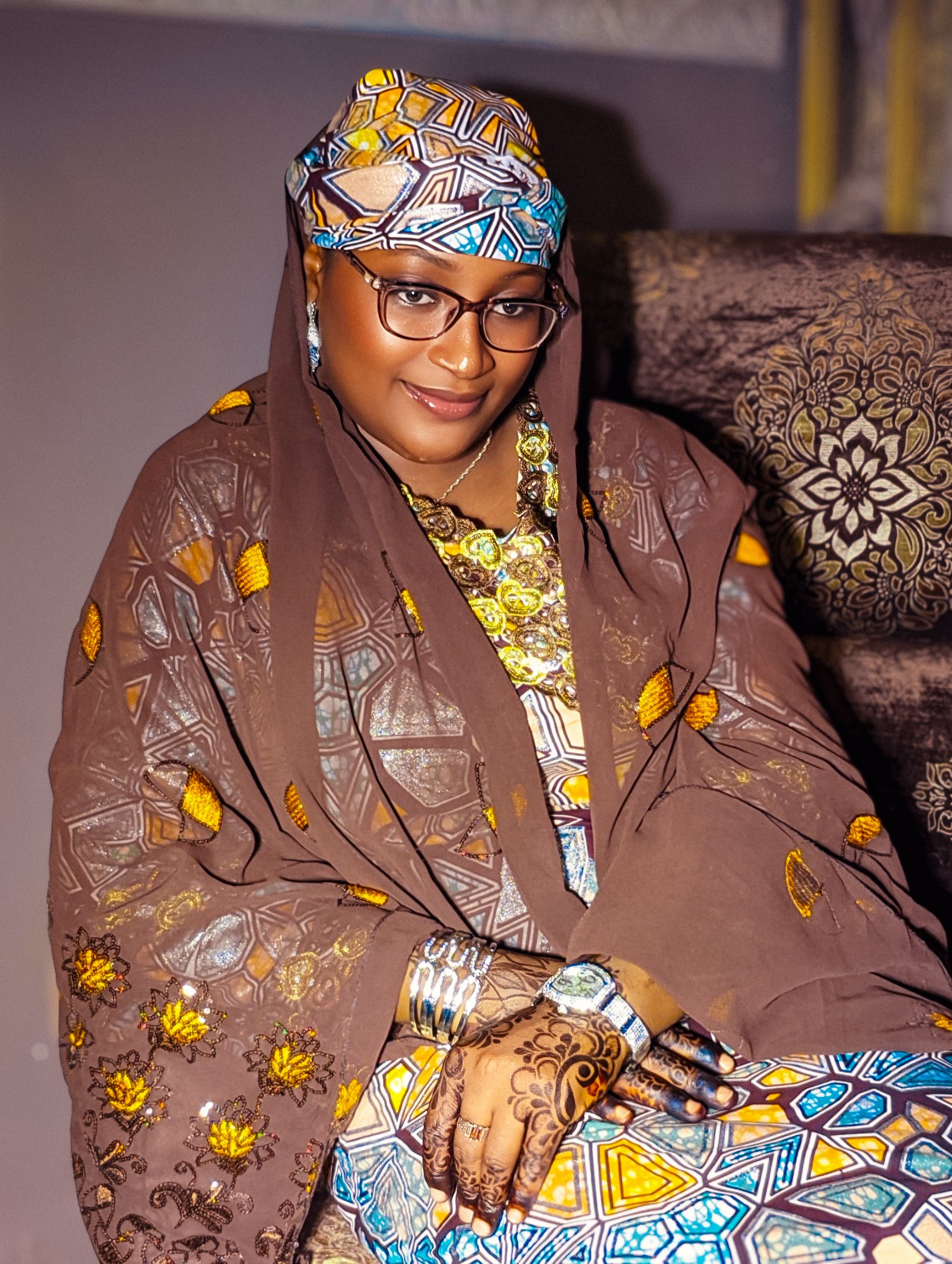 A woman in sophisticated Hausa attire with intricate patterns and vibrant colors.