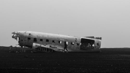 Free A stark image of a lone figure by the wreckage of a crashed aircraft on a desolate beach. Stock Photo