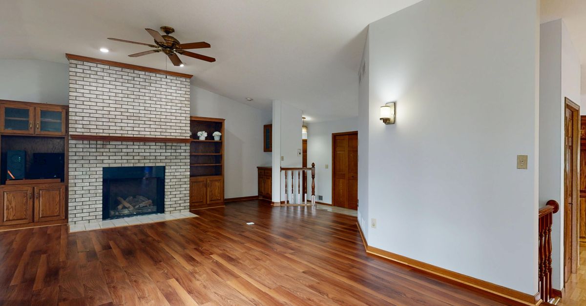 Bright and spacious living room featuring a brick fireplace, hardwood floors, and built-in cabinets.