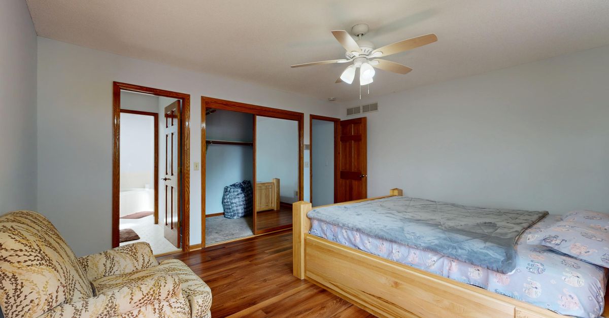Bright bedroom interior with wooden furniture and ceiling fan.