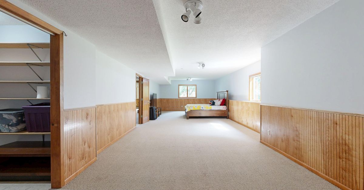 Empty basement room with wooden paneling and carpet, offering ample space for various uses.