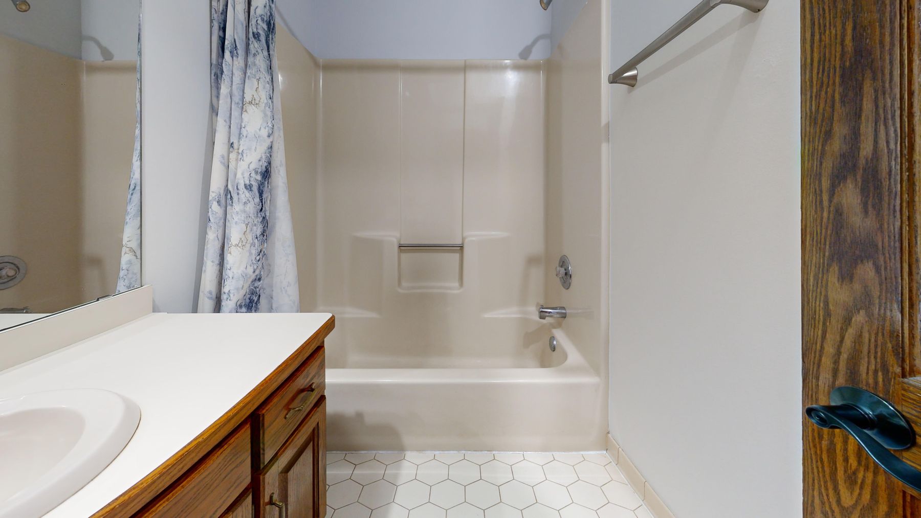 Compact modern bathroom with a vanity beside a clear glass shower and continuous pale surfaces