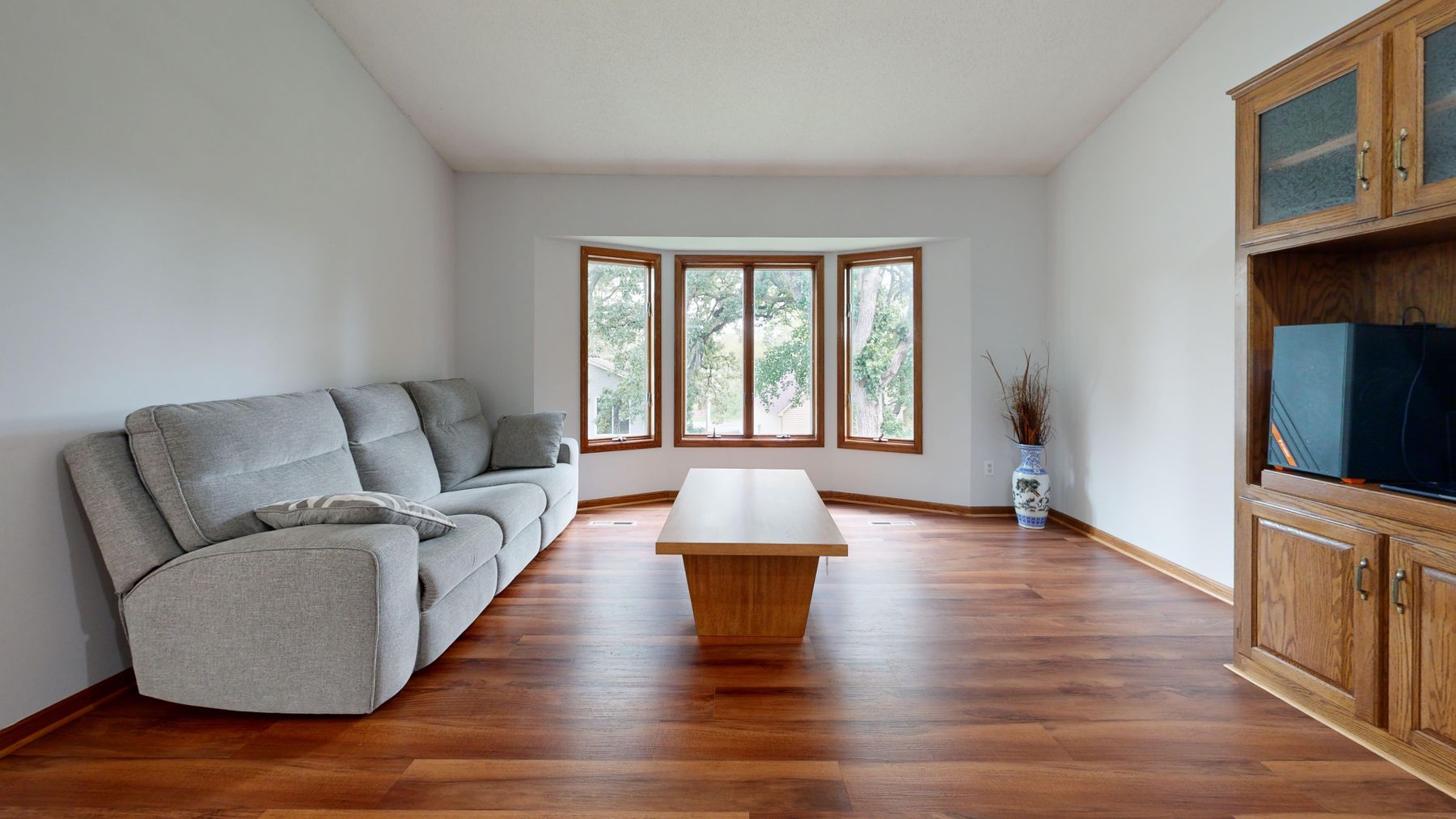 Light-filled apartment living room with large windows, pale walls and warm timber flooring