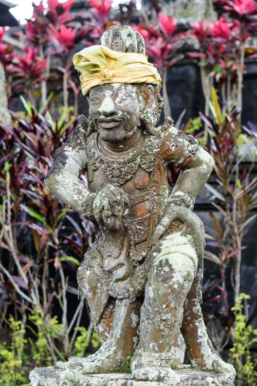 Free A traditional Balinese stone statue adorned with yellow fabric, set against vibrant foliage. Stock Photo