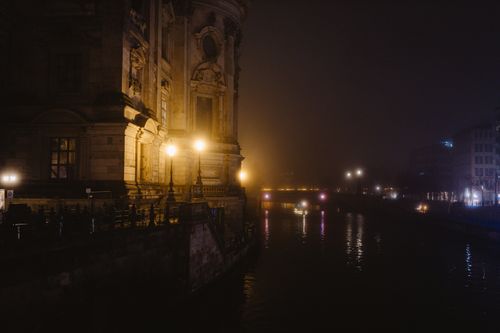 Free Night scene of a historic building by a river with glowing streetlights creating a moody ambiance. Stock Photo