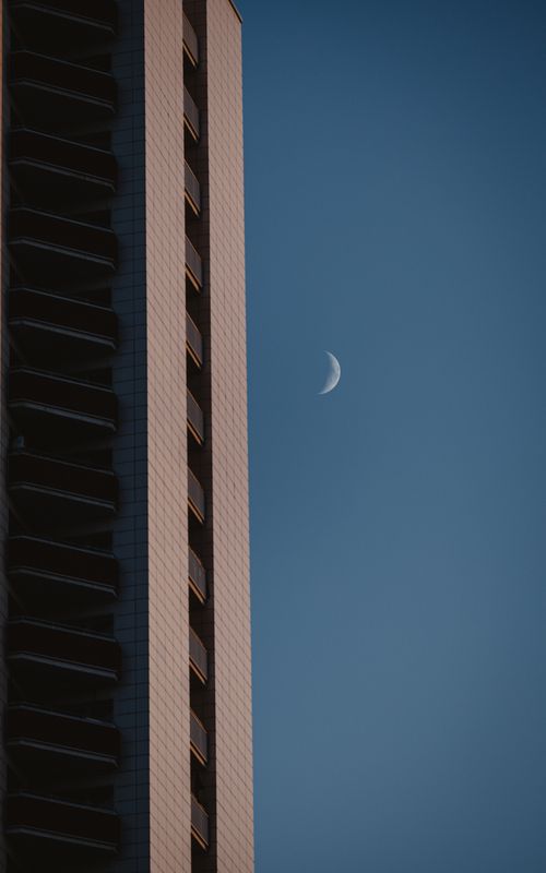 Free Minimalist view of a building facade with a crescent moon against a blue sky. Stock Photo