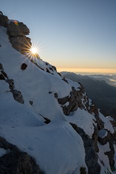 Stunning sunrise on a snowy mountain peak with clear skies and distant valleys.