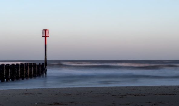 Serene coastal scene at Bridlington, England with a red beacon and smooth waves.