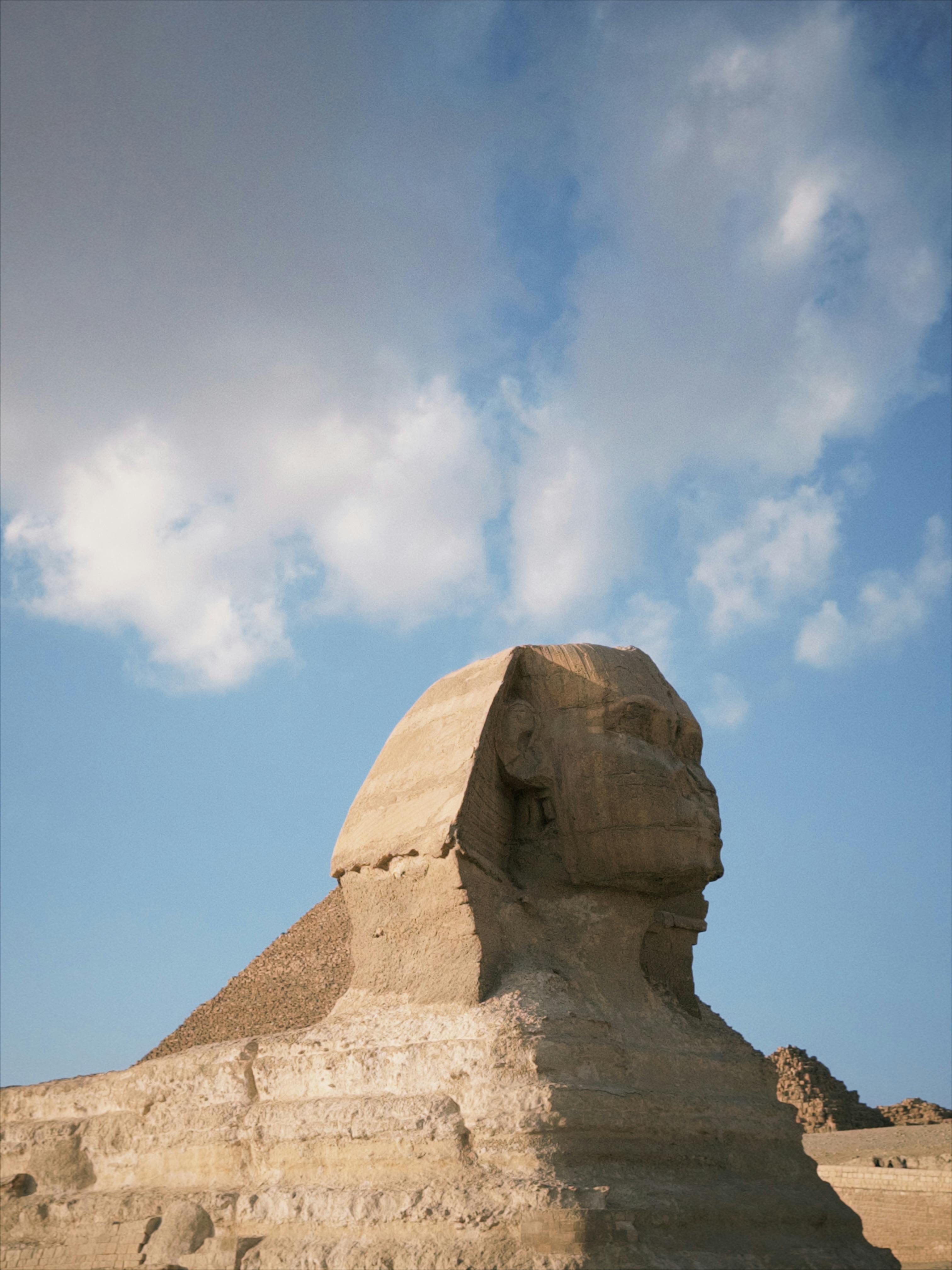 The iconic Great Sphinx of Giza set against a clear blue sky with fluffy clouds.