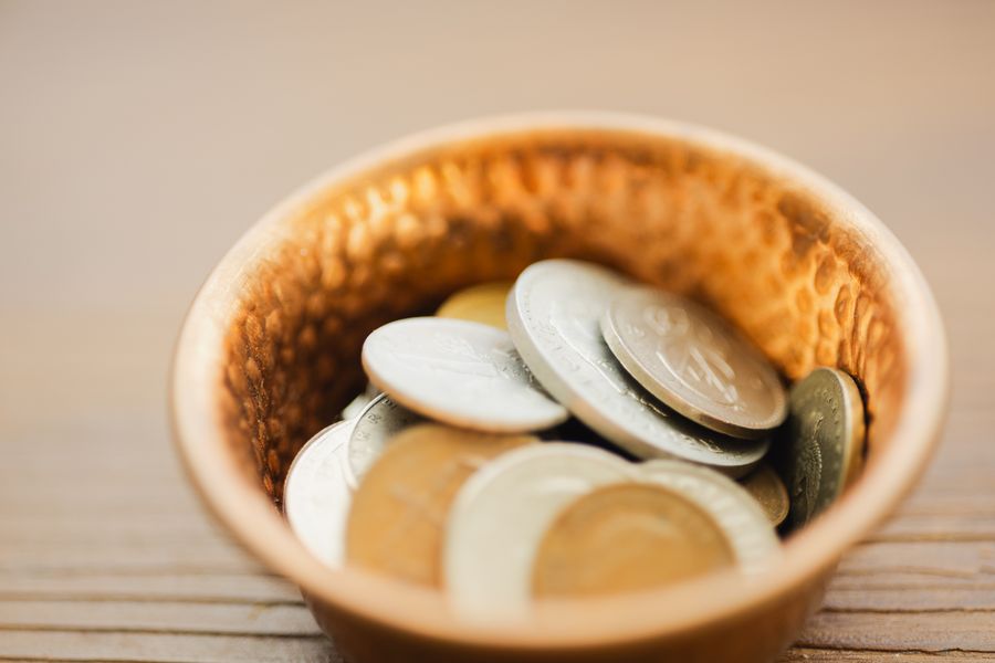 A detailed view of various coins in a vintage textured metal bowl, showcasing texture and currency.