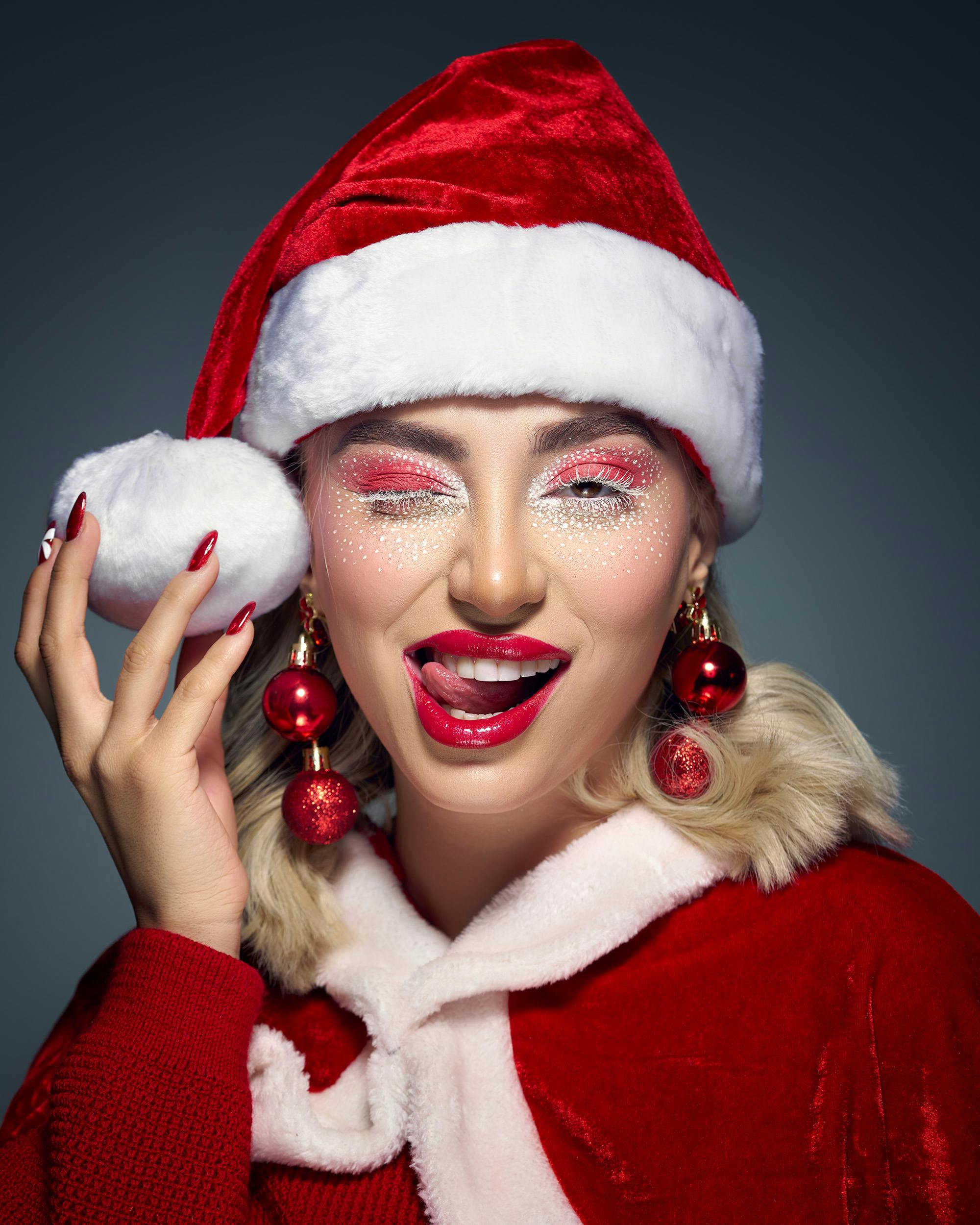 Kostenlos Eine lächelnde Frau mit Weihnachtsmütze, auffälligem Make-up und festlichen Ohrringen genießt die Weihnachtsstimmung. Stock-Foto