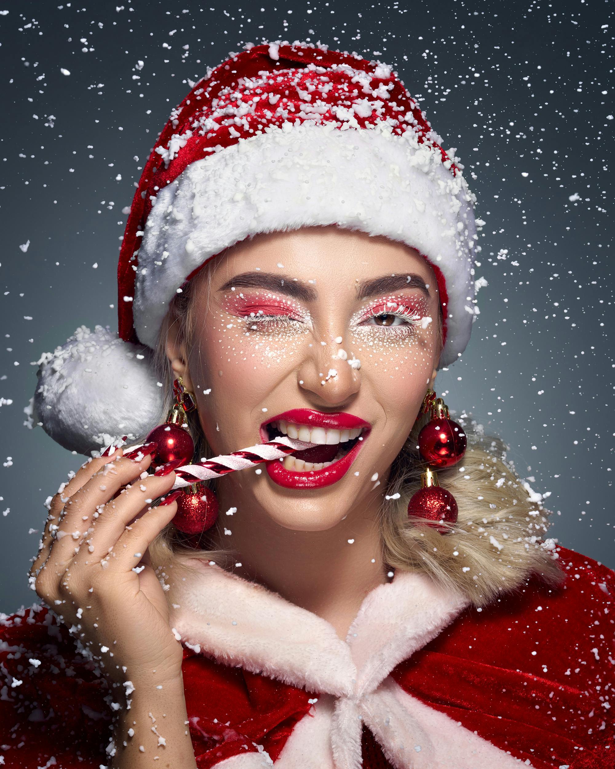 Gratis Mujer con gorro de Papá Noel y maquillaje festivo disfrutando de un bastón de caramelo. Foto de stock