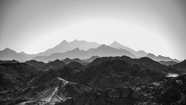 Black and white photo of rugged mountains with dramatic lighting creating an atmospheric perspective.