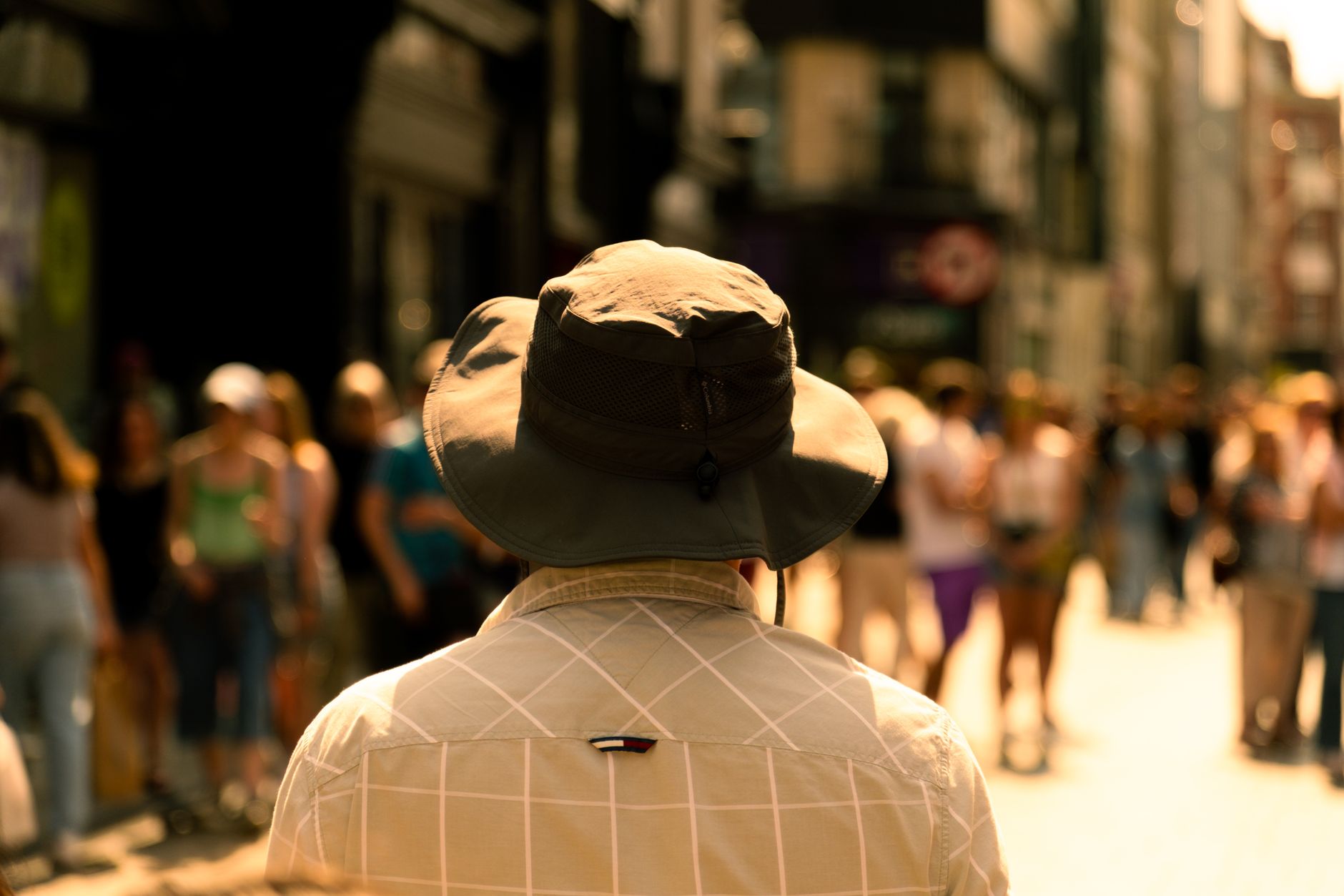 A scenic urban street capture featuring a sunlit pedestrian wearing a wide-brimmed hat during late summer.