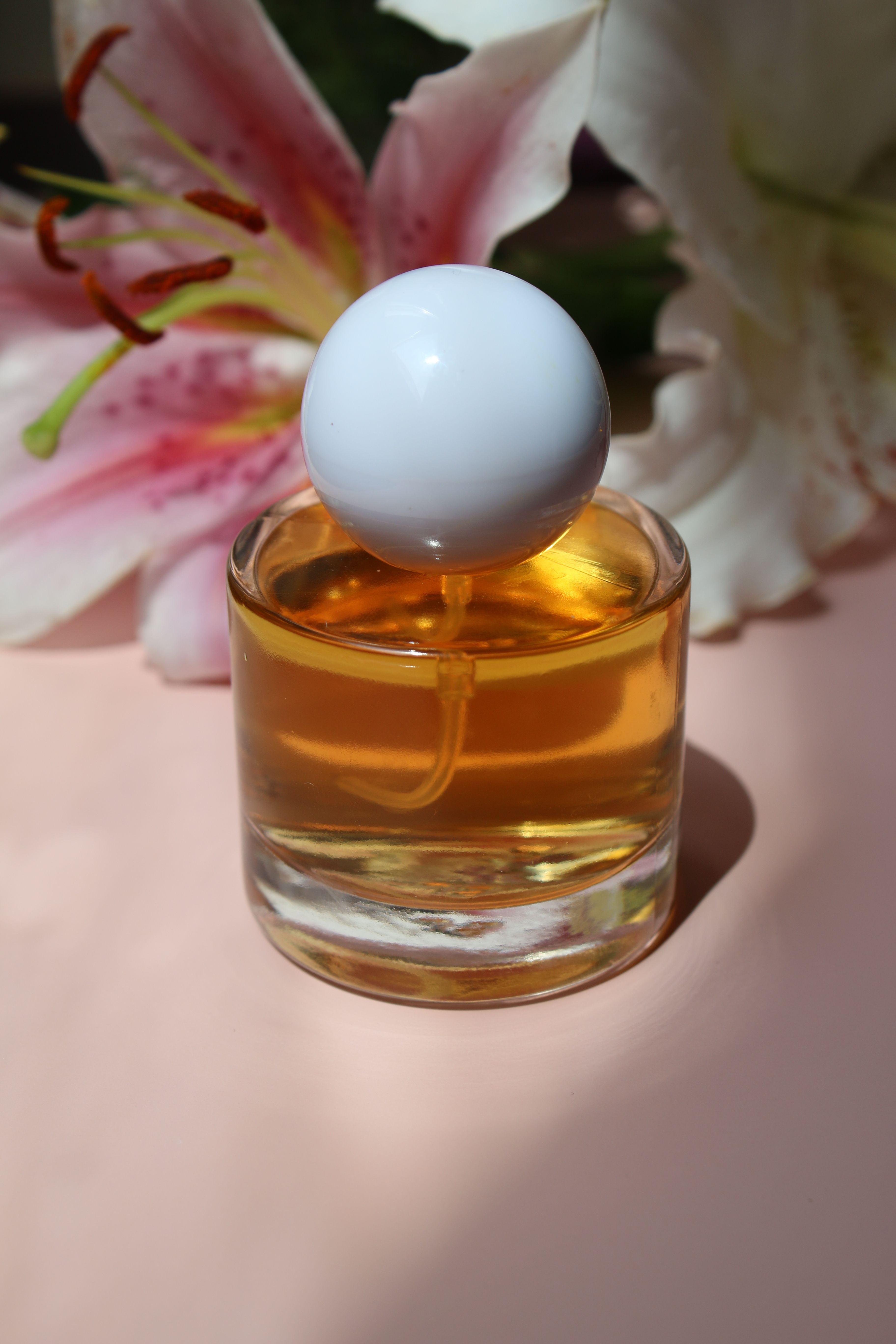 A stylish perfume bottle with white lilies in soft natural lighting, perfect for beauty themes.