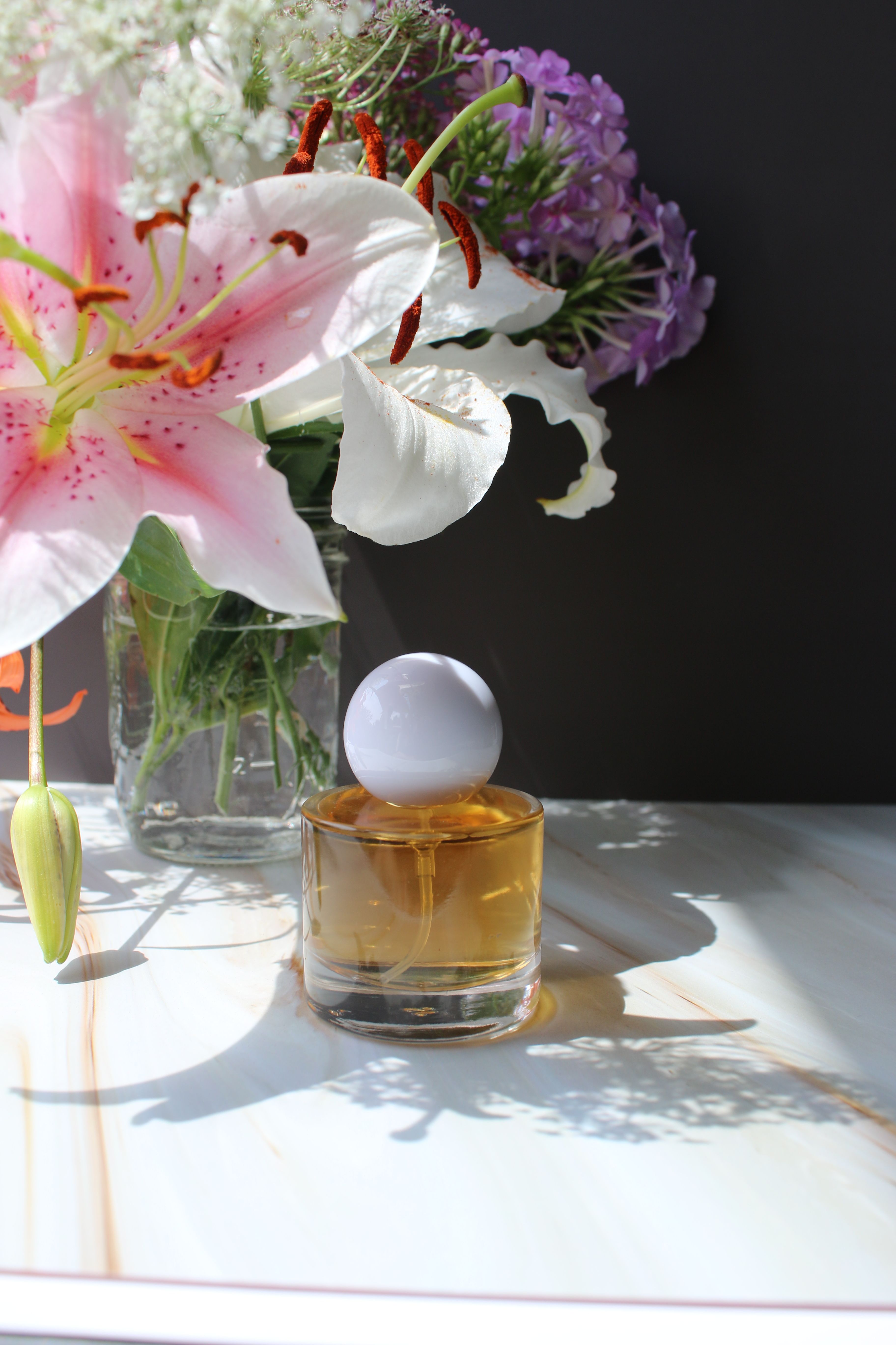 Perfume bottles beside fresh flowers in soft daylight