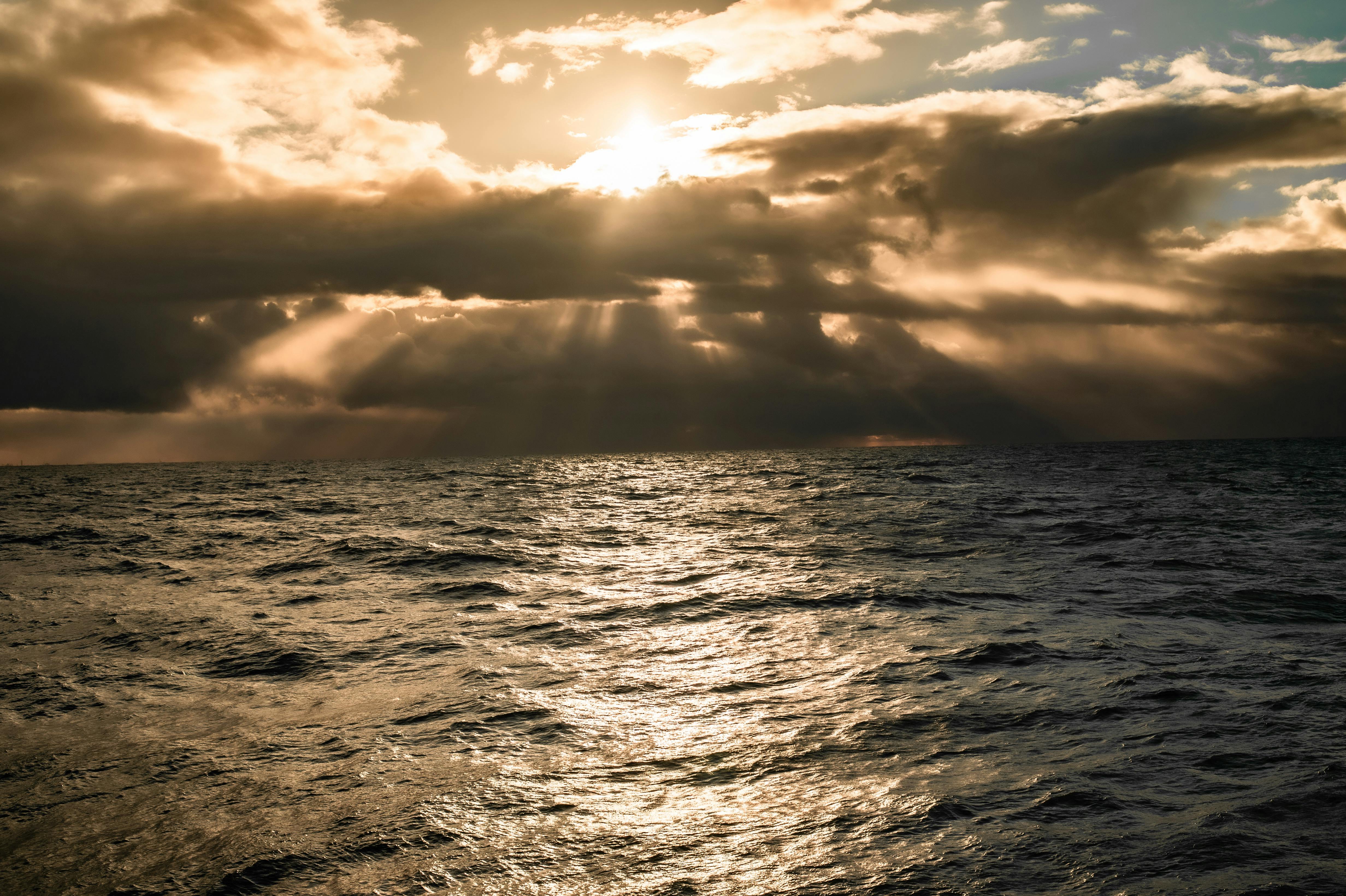 Gratis En fantastisk utsikt over solnedgangen over havet, med dramatiske skyer og solstråler. Arkivbilde