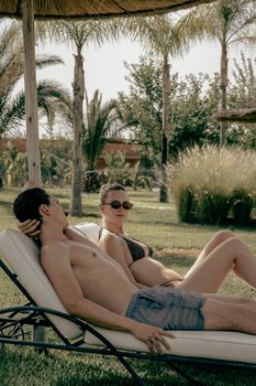 Young adults sunbathing by the poolside in Marrakesh, Morocco, enjoying a sunny summer day.