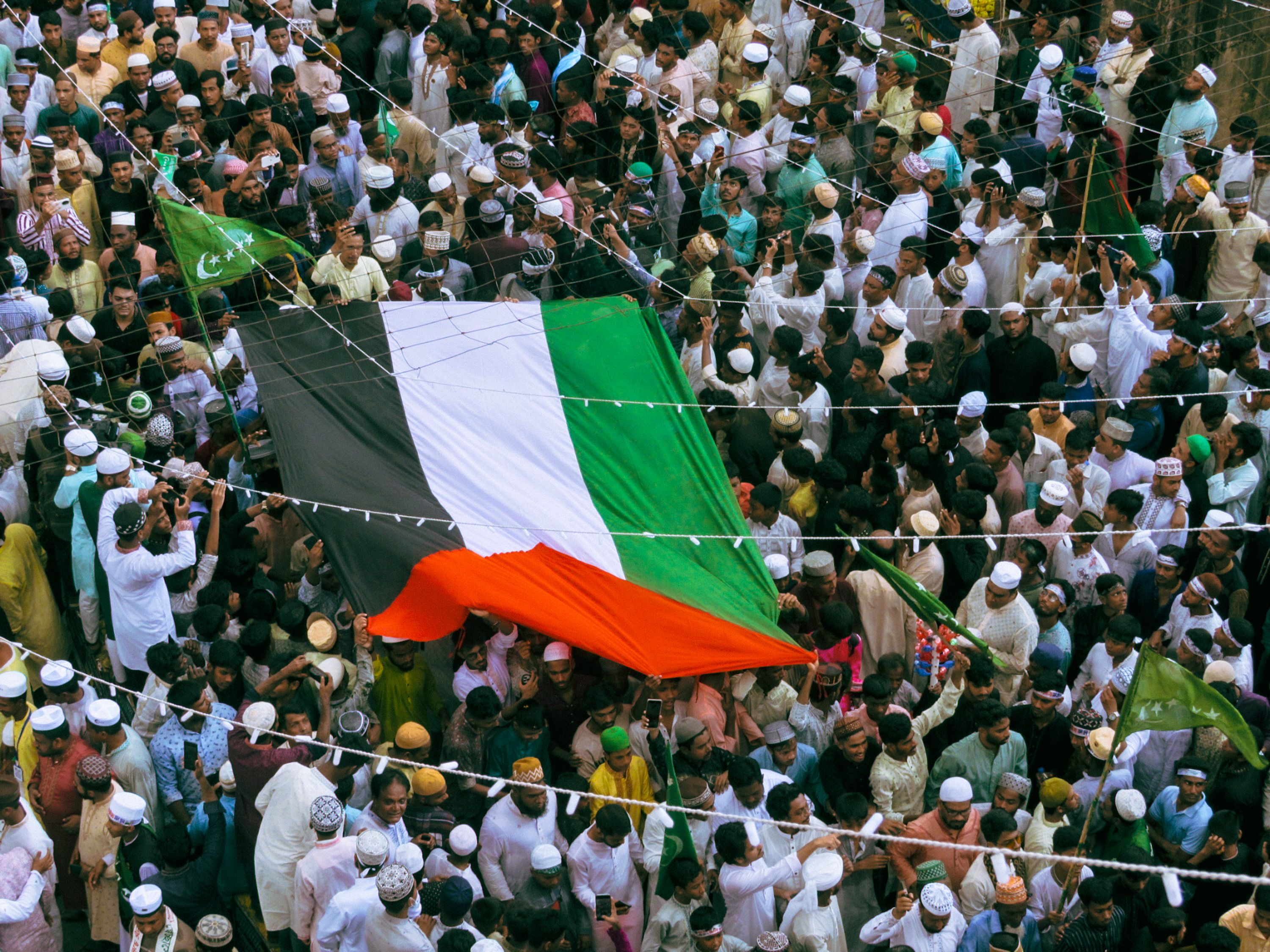 A crowd of people gathered in Chattogram, Bangladesh, celebrating with a large colorful flag.