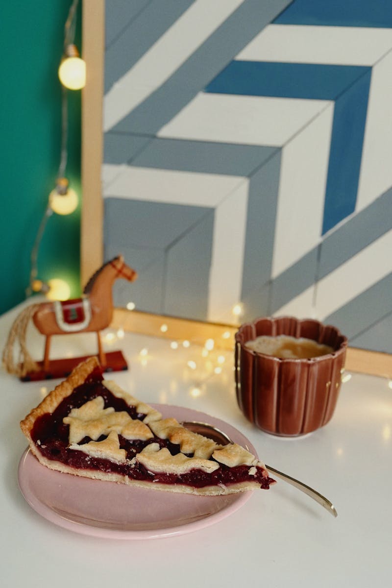 A delicious cherry pie slice with holiday decor and a warm drink setup.