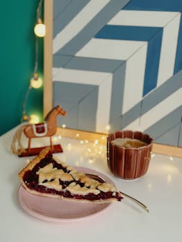 A delicious cherry pie slice with holiday decor and a warm drink setup.