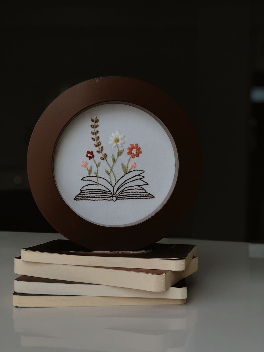 Botanical embroidery hoop with stitched leaves beside an open book