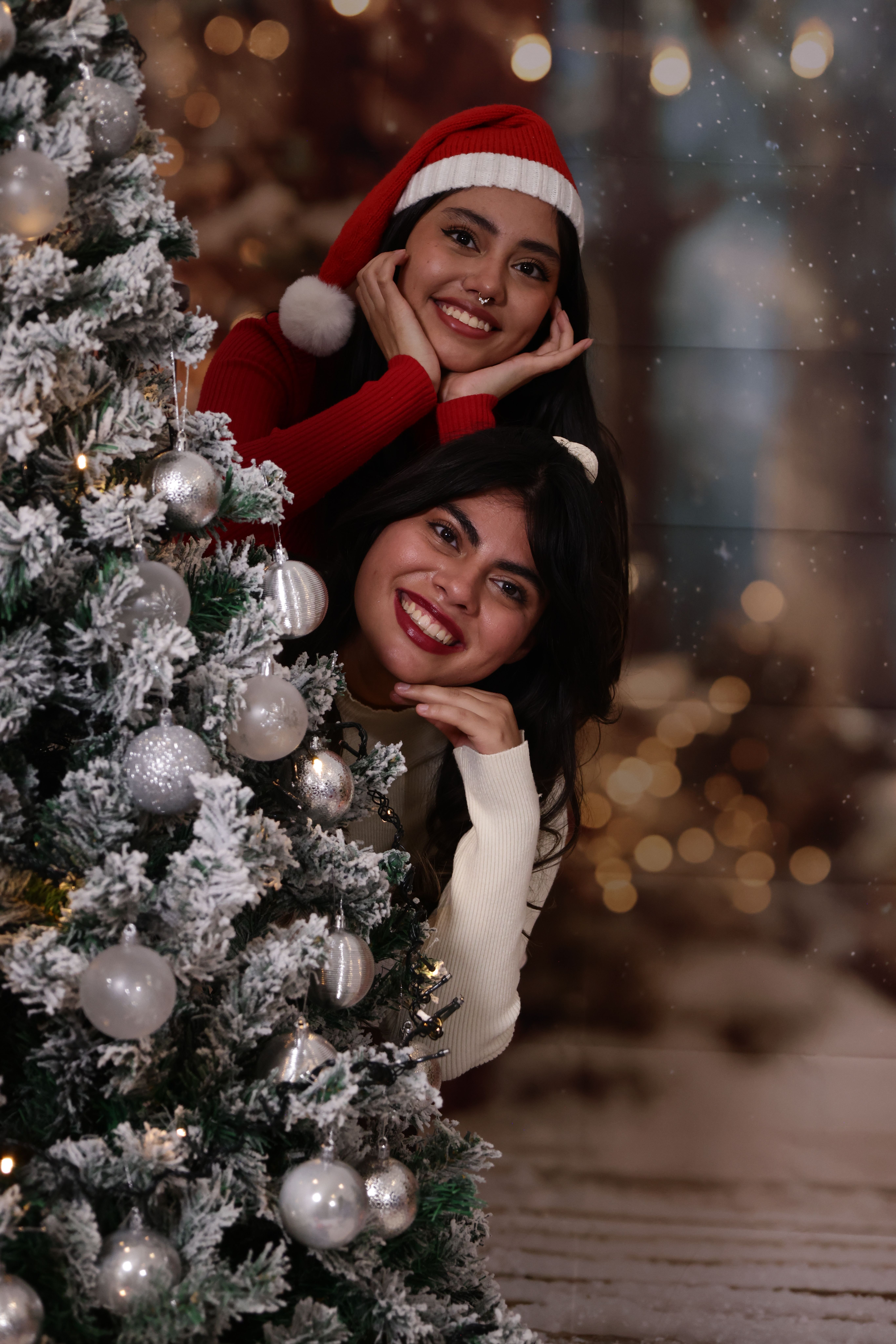 Fotomural Dos mujeres alegres celebrando la Navidad junto a un árbol decorado en el interior.