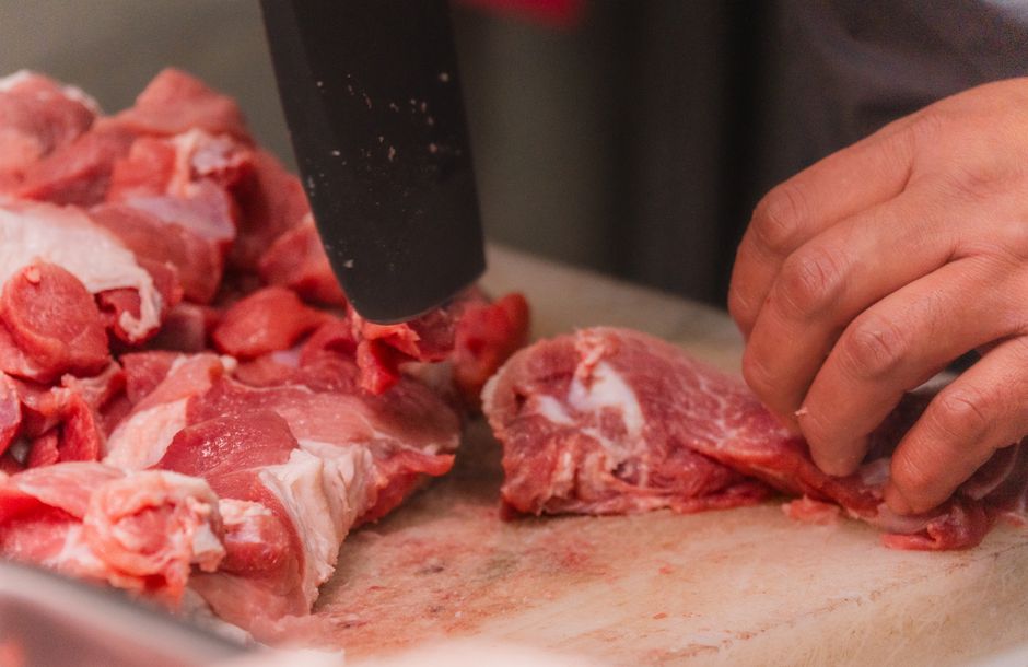 Close-up view of hands cutting raw meat with a knife on a chopping board, ideal for culinary or food safety topics.