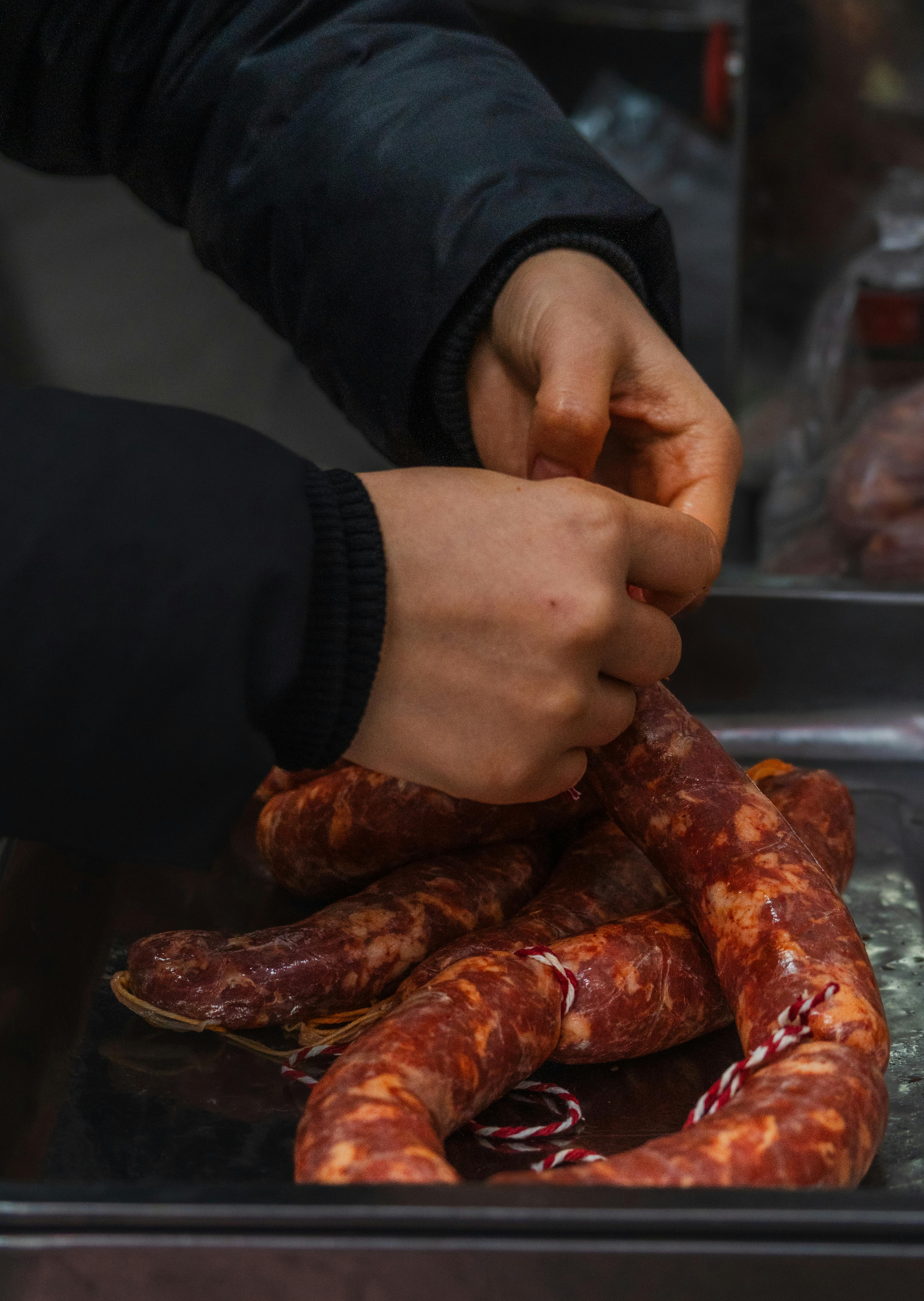 Close-up of hands preparing traditional spicy sausages on a metal tray, indoors.