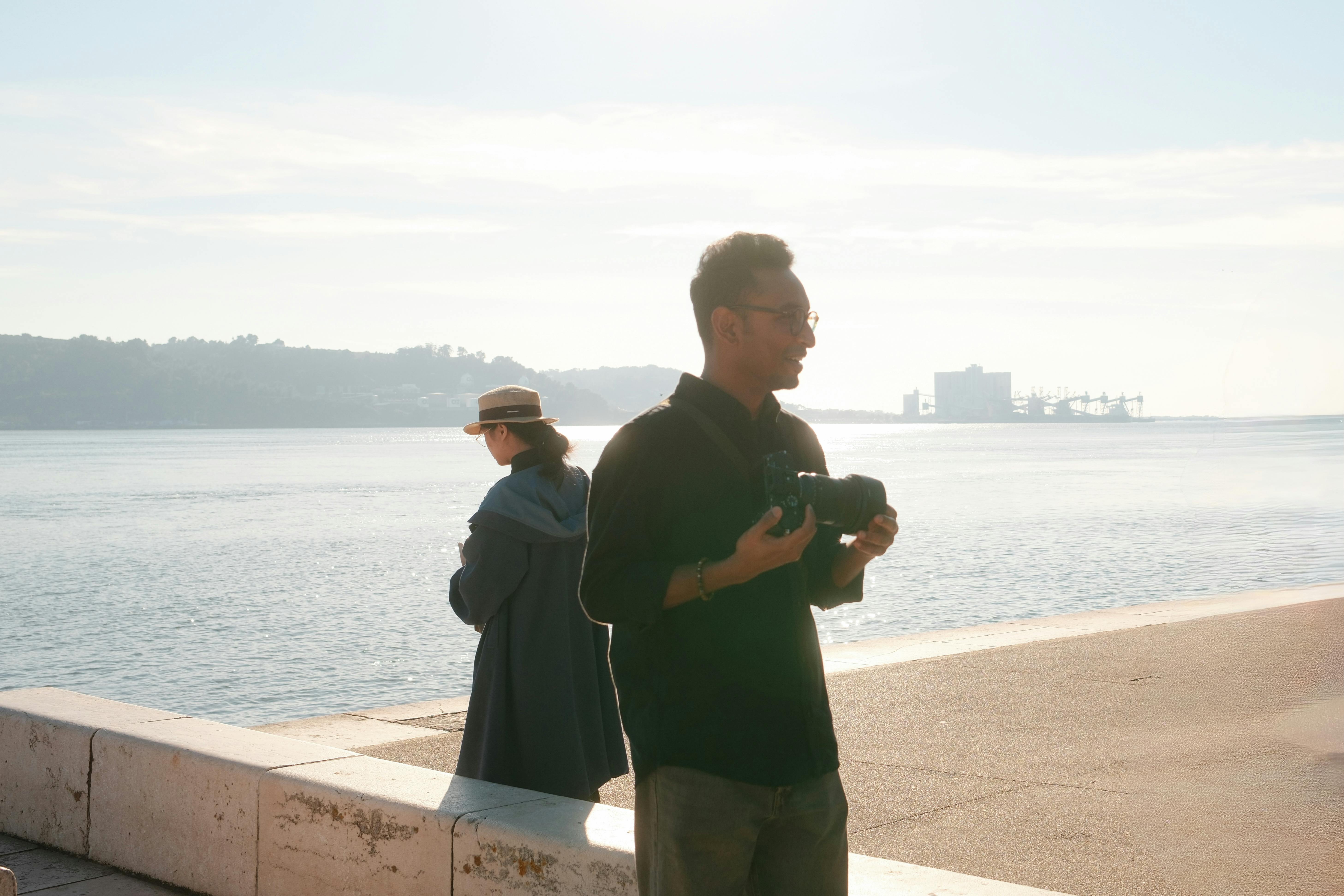 A serene moment capturing two photographers by the Lisbon waterfront during sunrise.