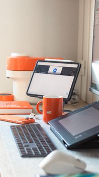 A sleek workspace setup with orange accents, featuring a tablet, keyboard, and mug.