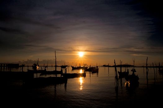 Tranquil sunset scene with silhouette of boats on calm water reflecting the golden sun.