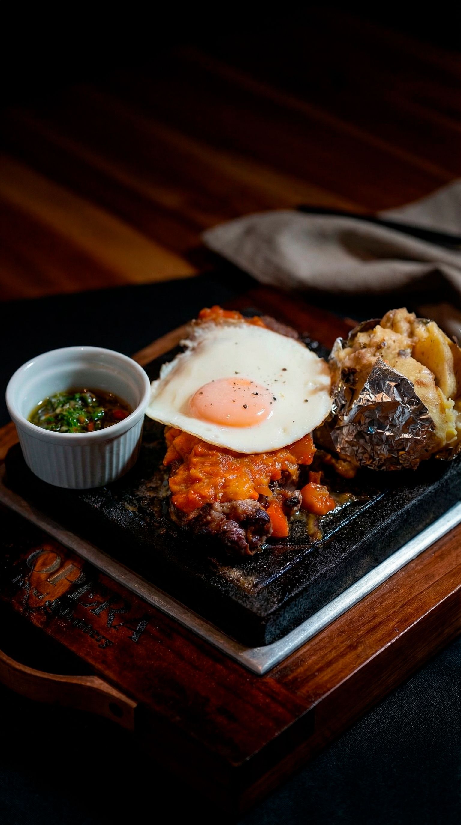 Savory Colombian-style sizzling steak topped with egg, served with baked potato and sauce.