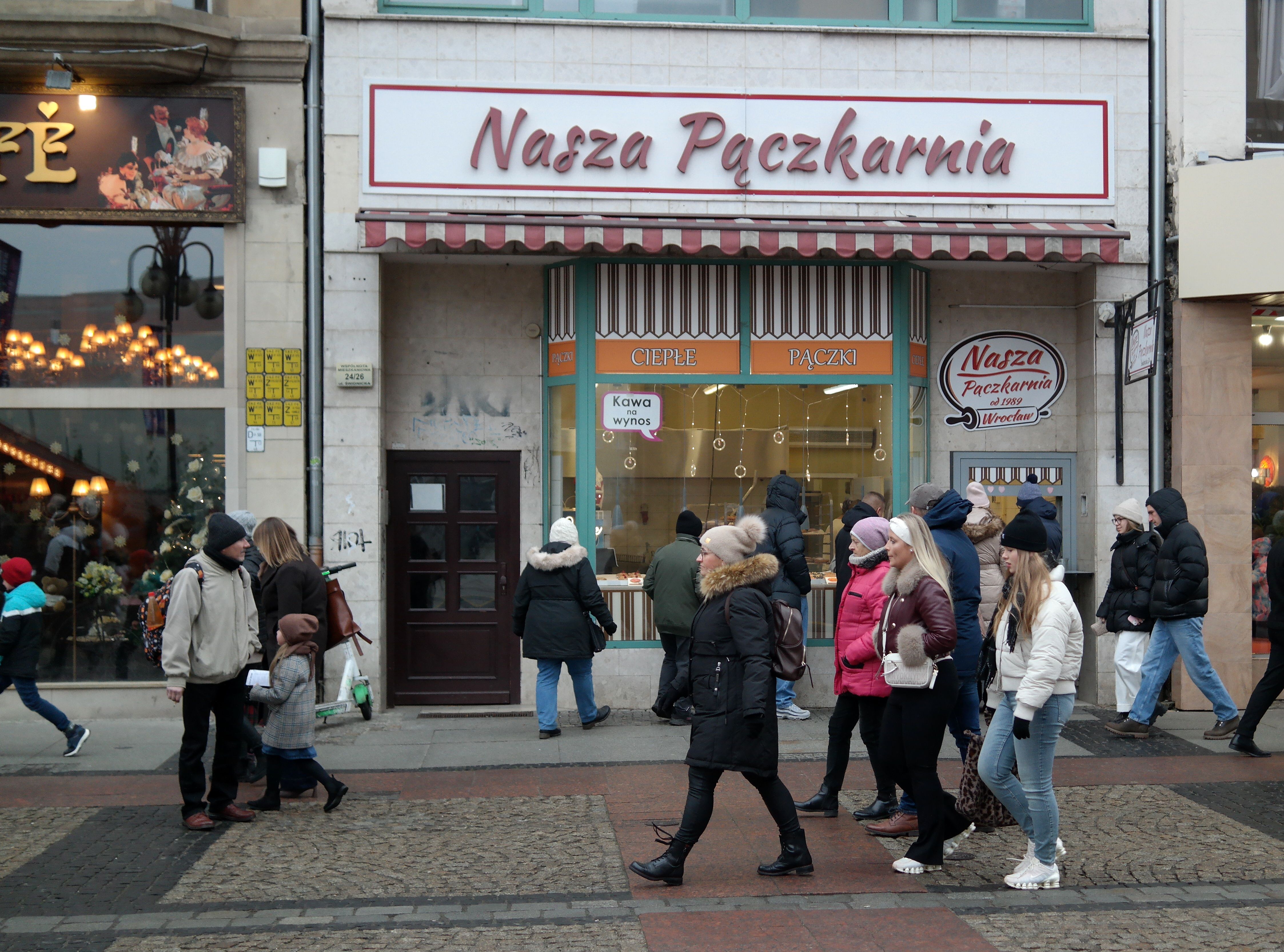 A lively street view with people passing by a famous bakery in winter.
