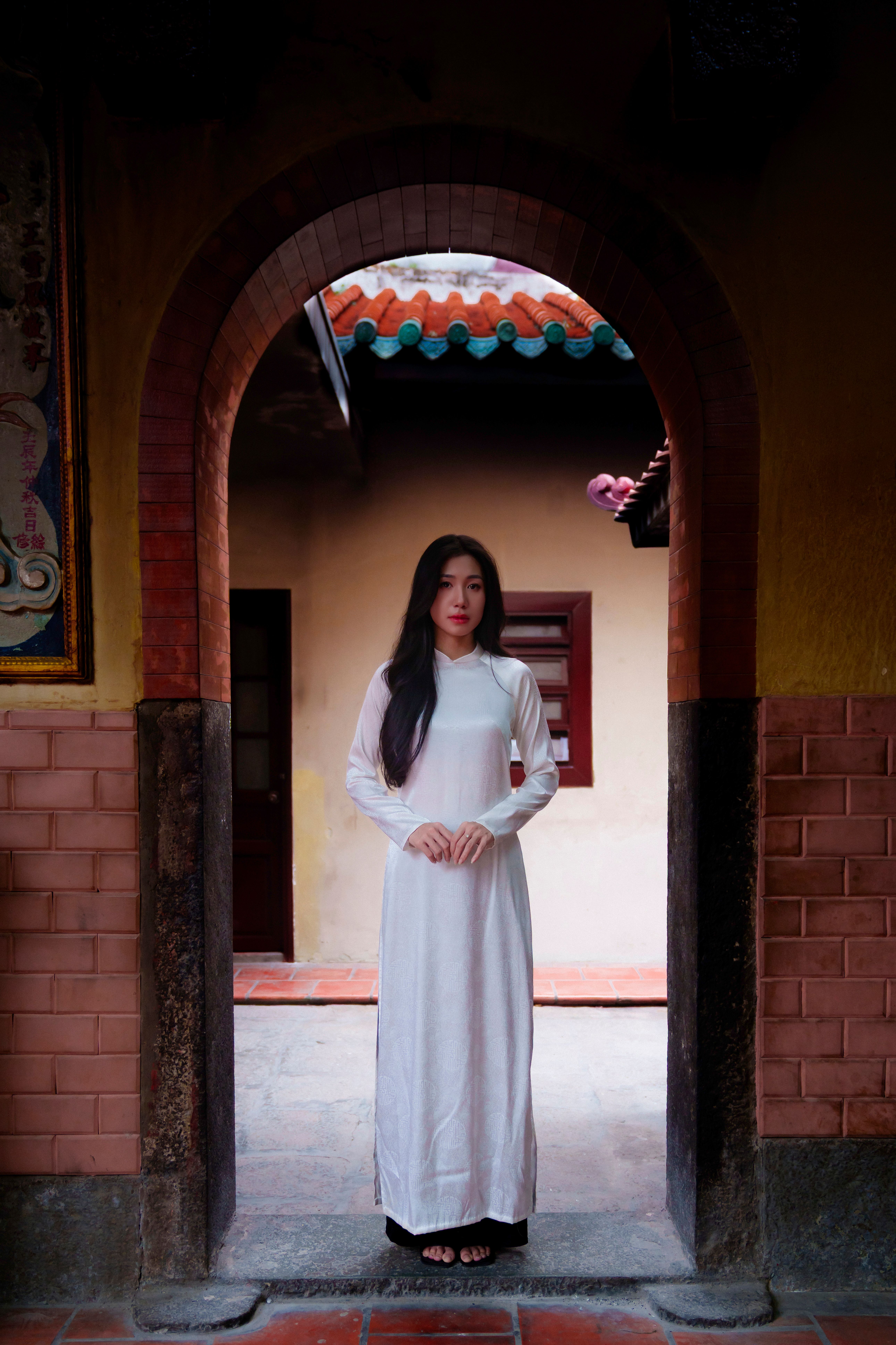 A woman in a traditional white Ao Dai stands in a temple archway, exuding elegance.