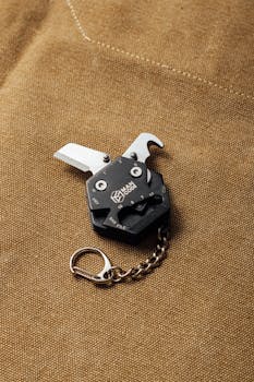 A sleek, black multi-tool with a chain on textured brown fabric, showcasing its portability and design.