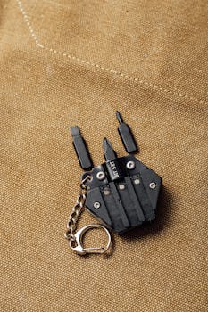 A small black keychain multi-tool with screwdriver bits on brown textile background.