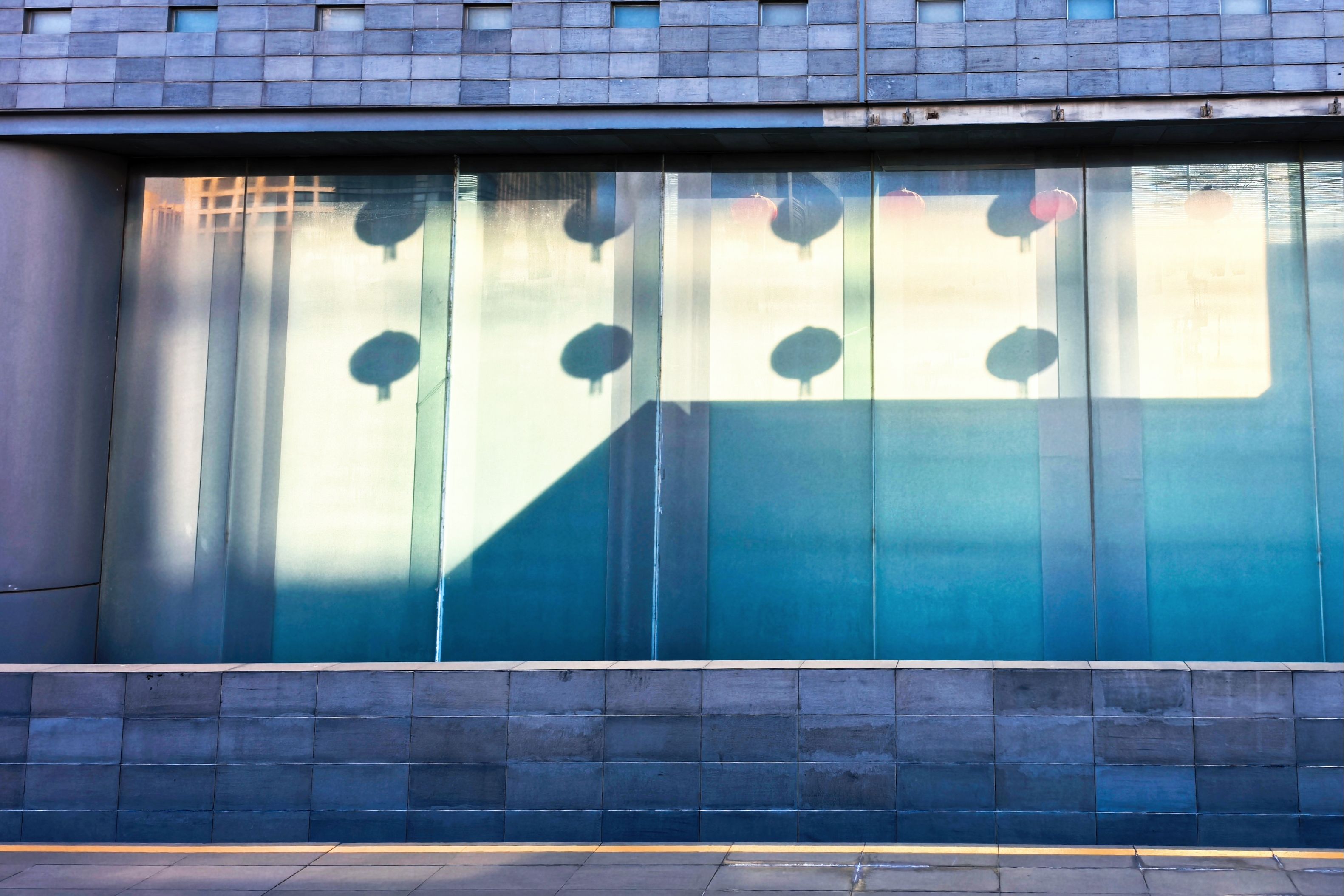 Shadows of lanterns cast on a modern glass building facade creating an abstract geometric pattern.