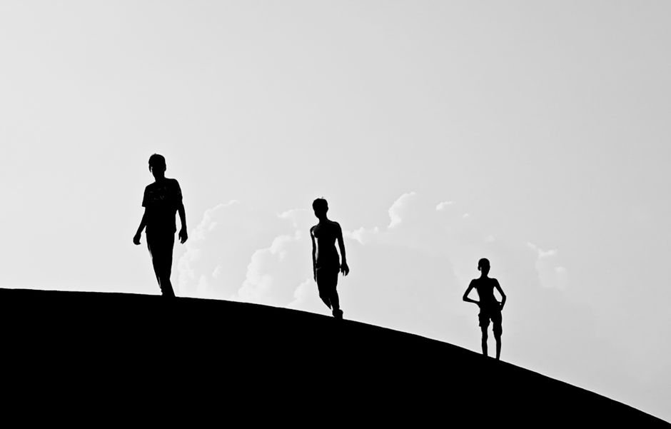 Three silhouetted figures walking on a hill with a bright sky backdrop in Dhaka, Bangladesh.