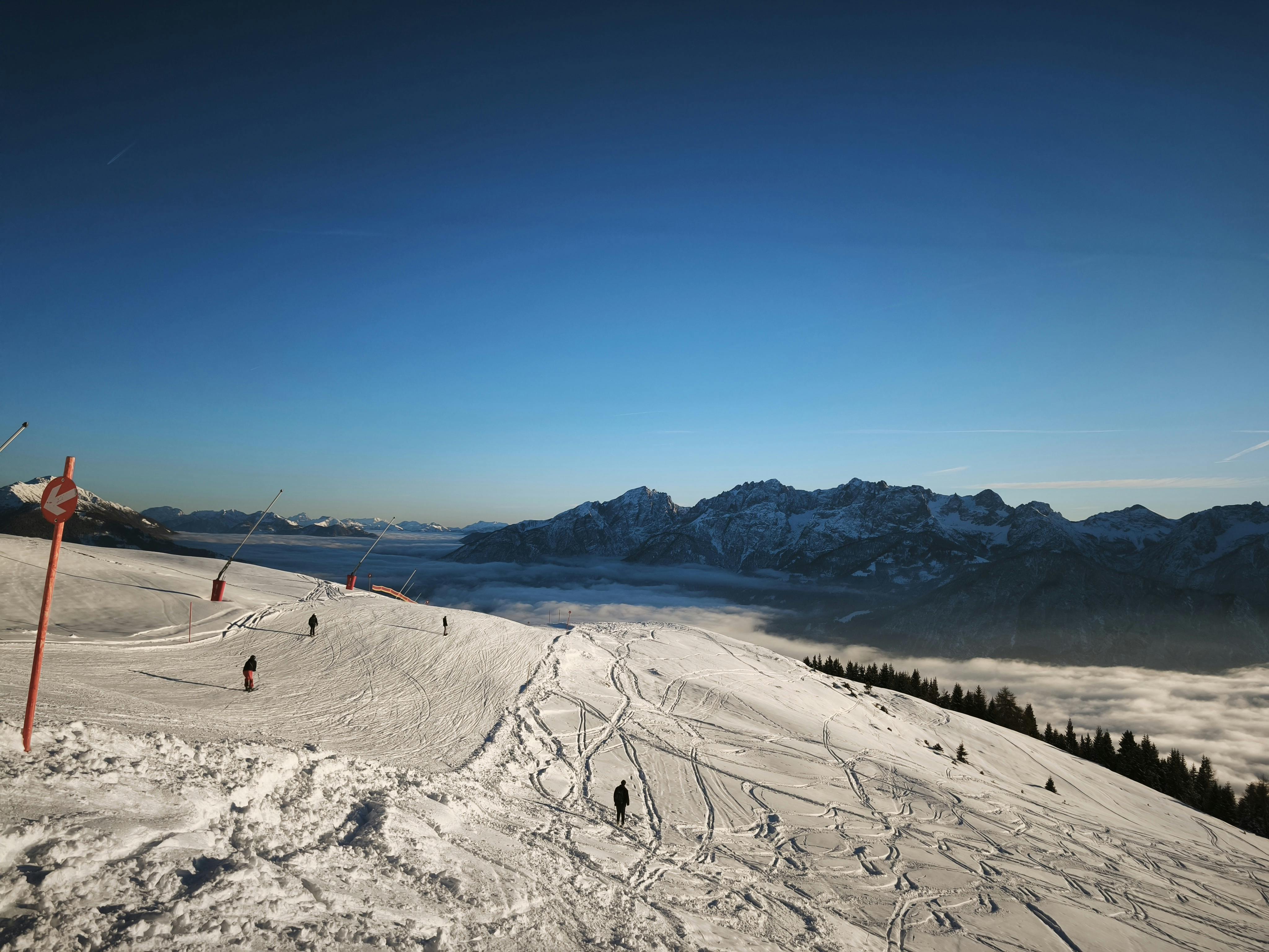Picturesque ski slope with skiers, snow-covered peaks and a clear blue sky.