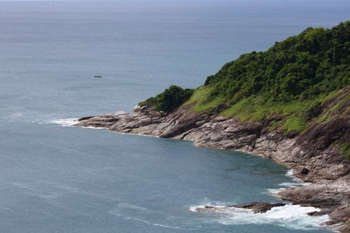 Free A picturesque view of a rocky coastline with lush greenery and ocean waves. Stock Photo
