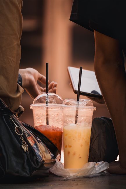 Two cold drinks with people interacting casually outdoors during the day.