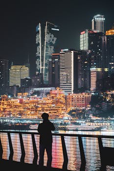 Stunning night view of Chongqing skyline featuring a silhouetted figure overlooking illuminated skyscrapers.